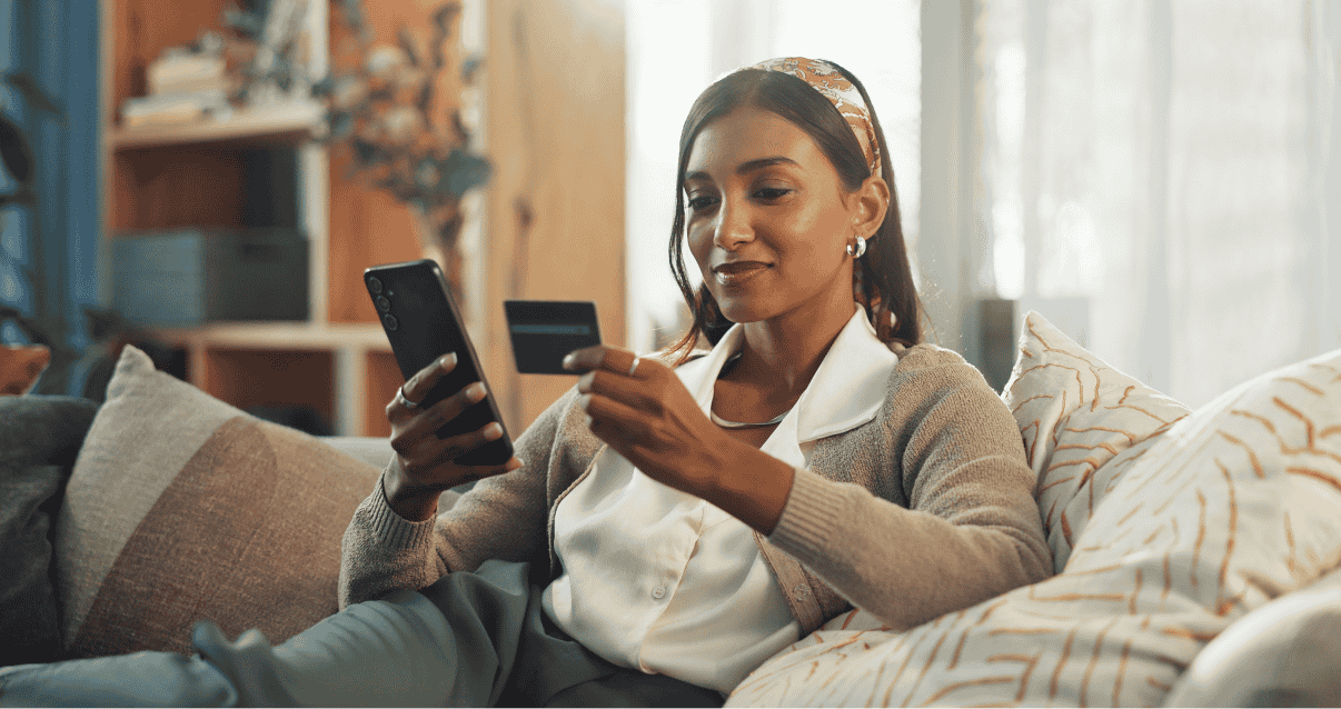 Woman sitting on a sofa looking at a phone and credit card. 